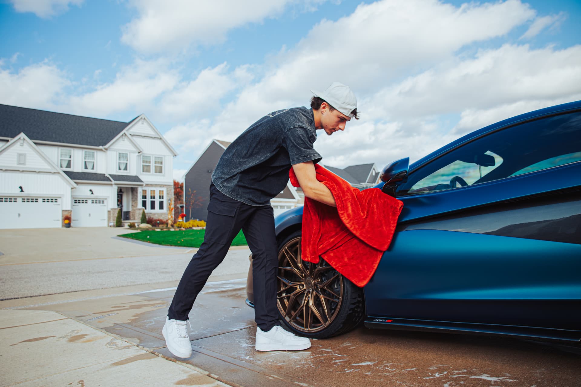 Detailer drying a blue sports car with a red towel